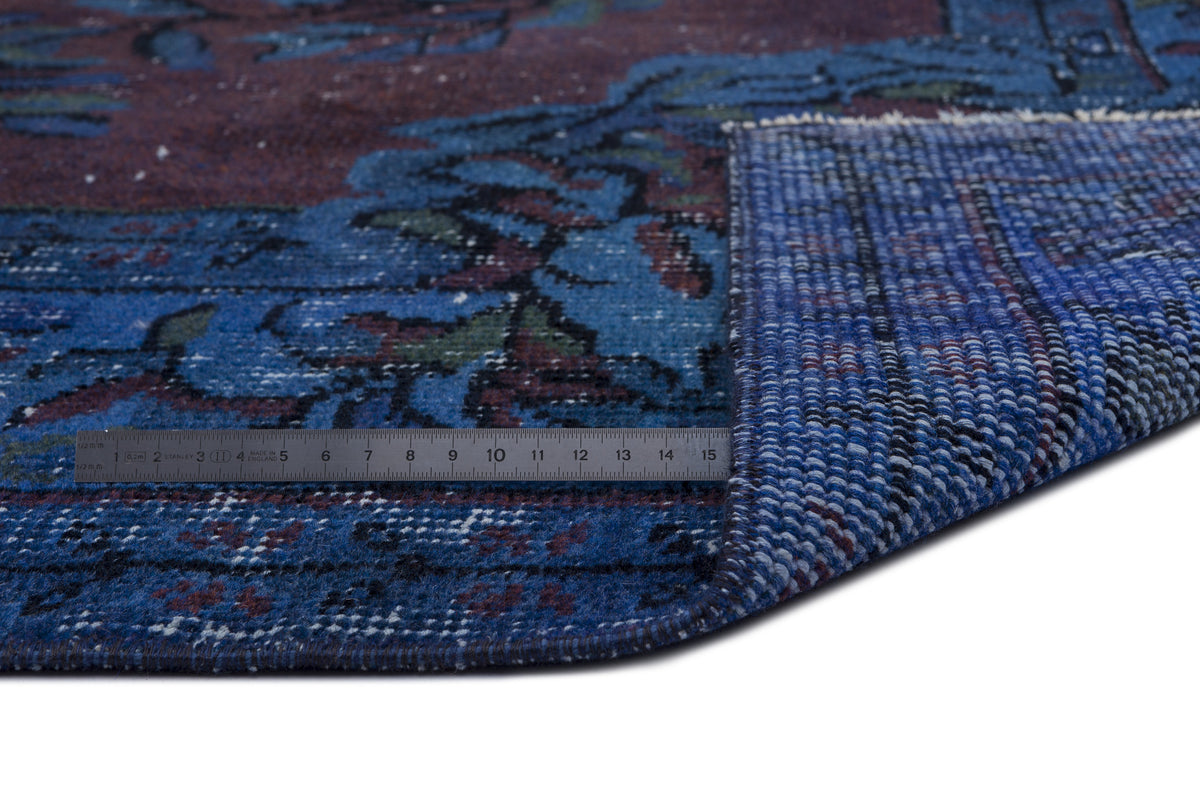 Blue and burgundy traditional patterned rug with a corner folded over, showing the woven backing and a metal ruler.