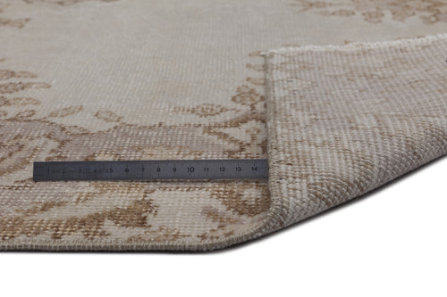 Load image 1 in gallery view. Beige and cream vintage-style rug with a faded floral medallion pattern, shown with a corner folded and a metal ruler.