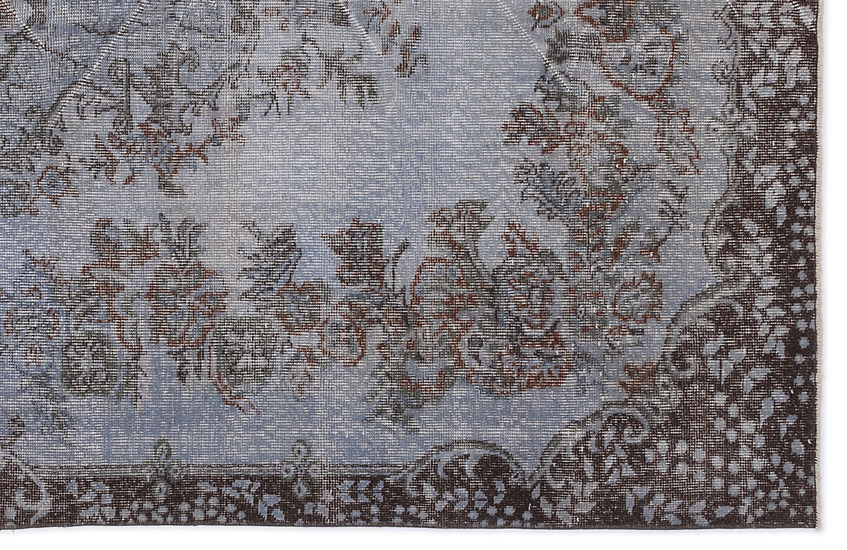 Distressed light blue rug with a dark brown floral medallion pattern and ornate border.