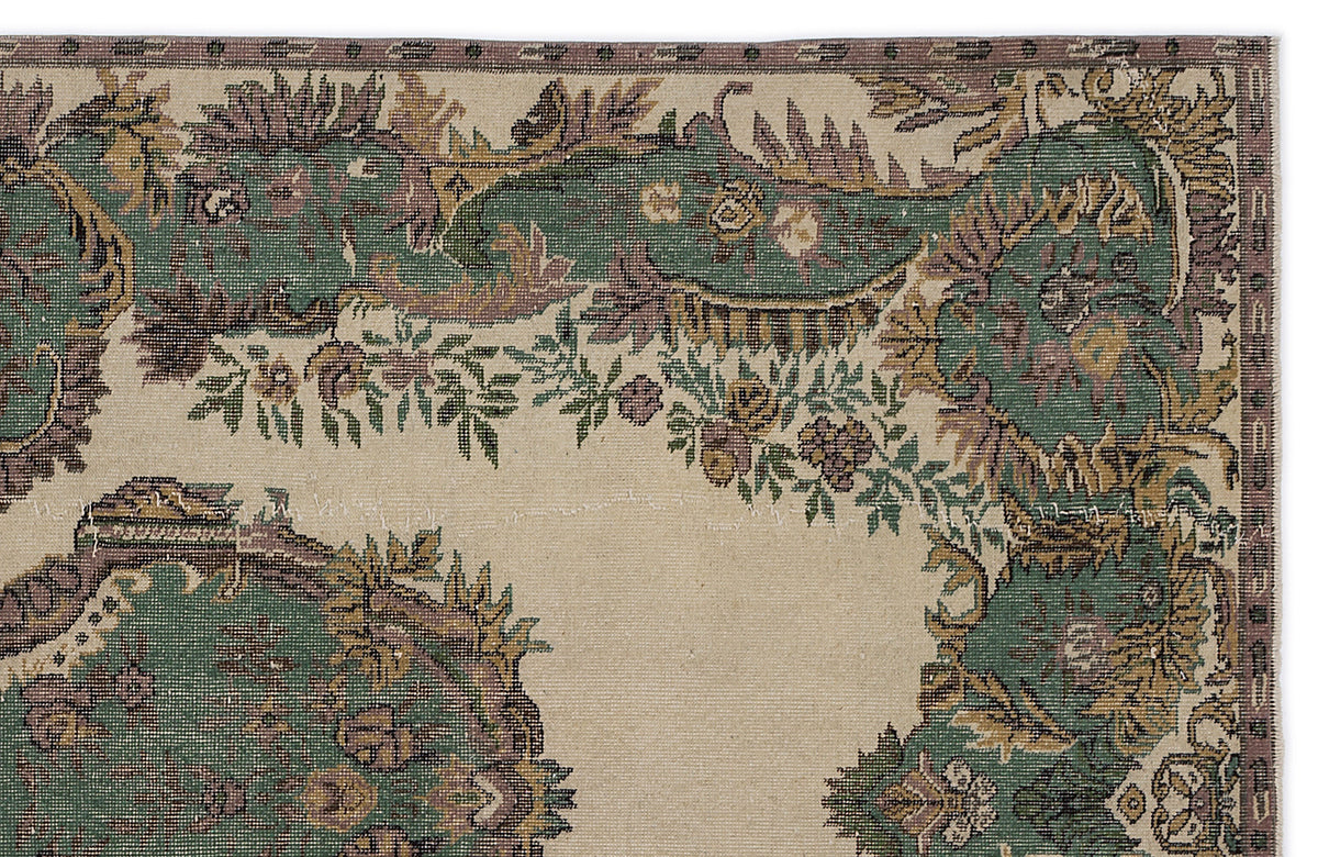Beige rug with a distressed green and purple floral medallion pattern and a decorative border.