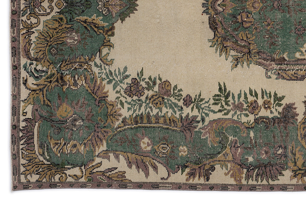 Beige rug with a distressed green, brown, and purple floral medallion pattern and a decorative border.