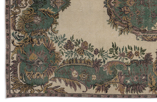 Load image 1 in gallery view. Beige rug with a distressed green, brown, and purple floral medallion pattern and a decorative border.