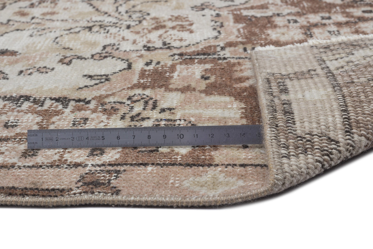 Beige and brown vintage-style rug with a distressed floral pattern, shown with a metal ruler for scale.