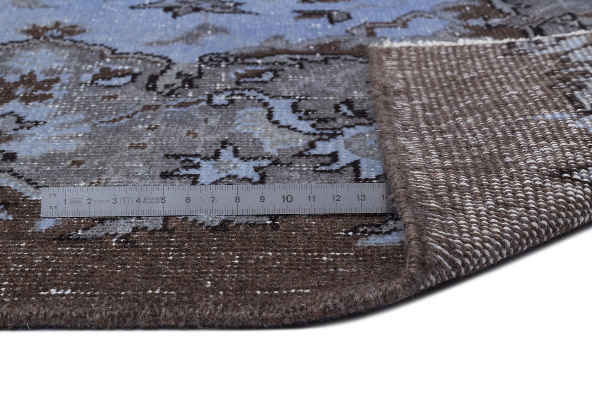 Blue and brown distressed floral rug with a folded corner showing the woven backing and a metal ruler for scale.