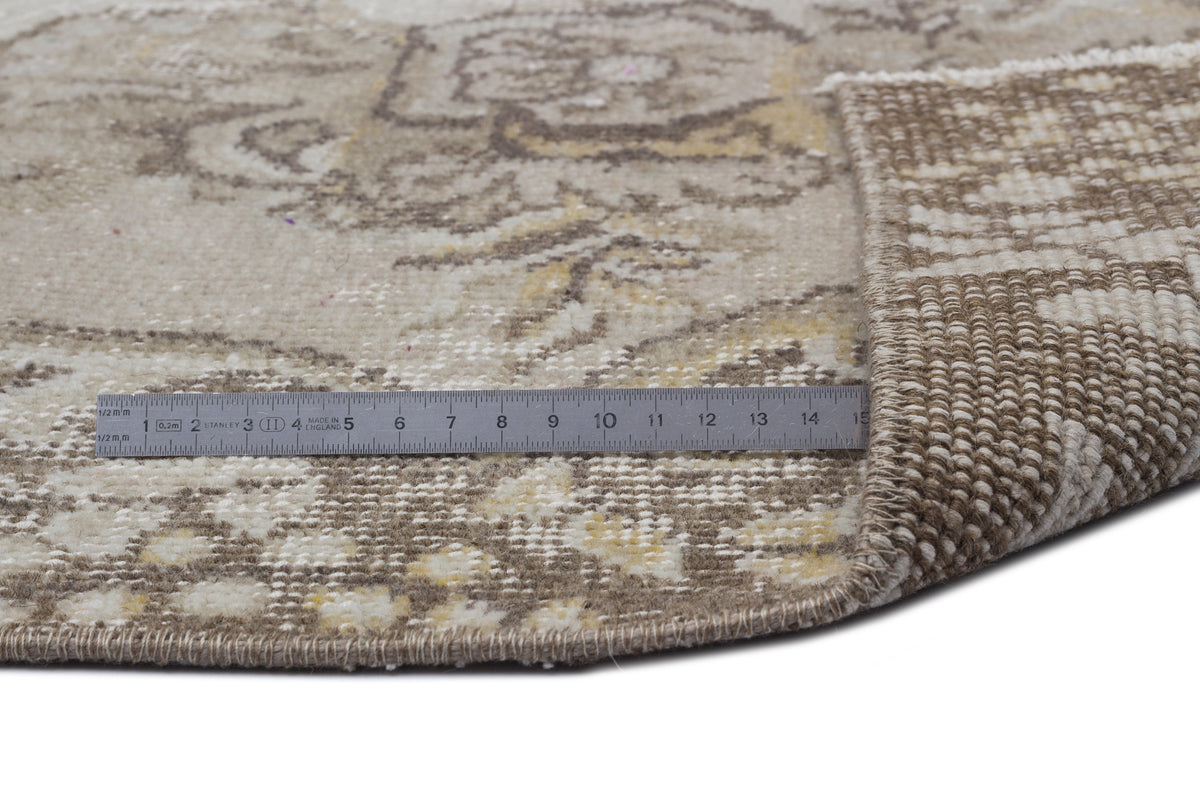 Beige and cream vintage-style rug with a faded floral medallion pattern, showing the woven backing and a metal ruler.