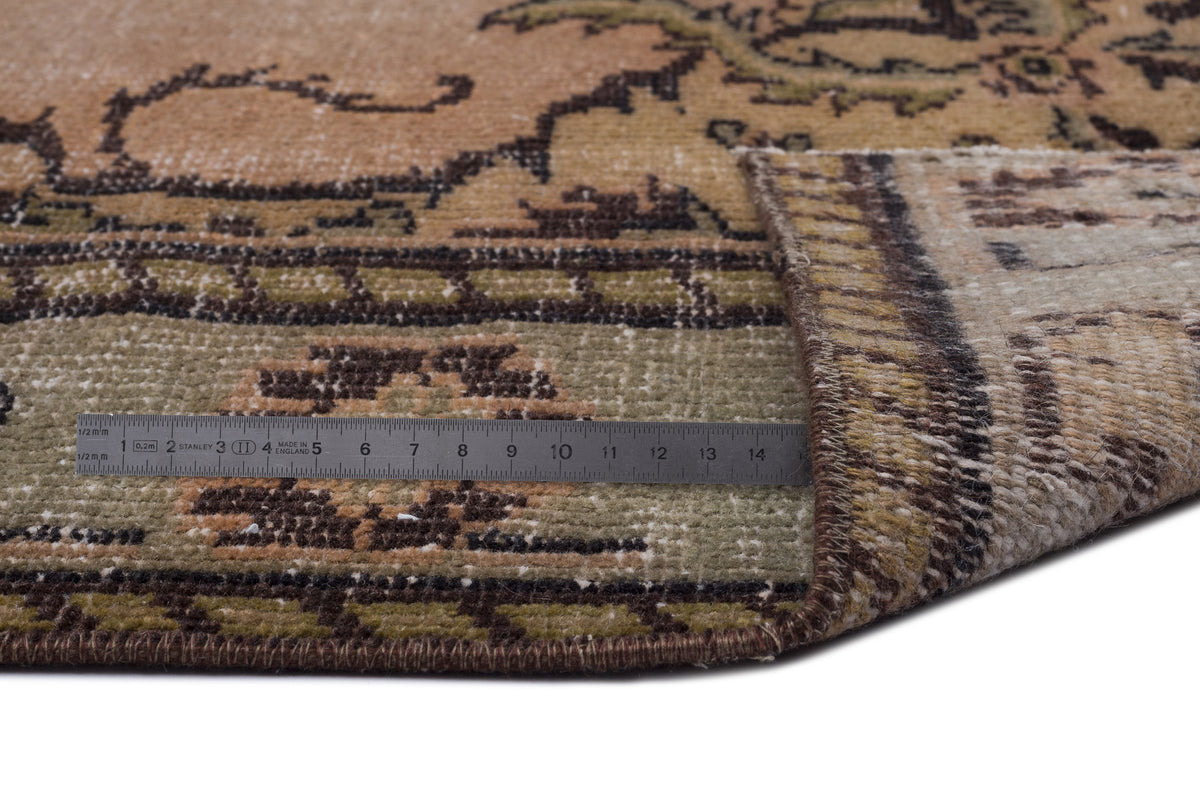 Tan, olive, and brown vintage-style rug with a floral border, shown with a metal ruler for scale.