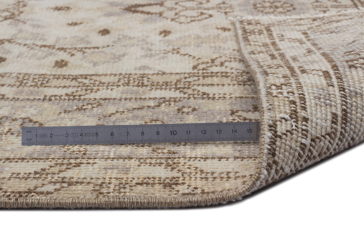 Beige and cream distressed traditional rug with a folded corner and a metal ruler for scale on a white background.