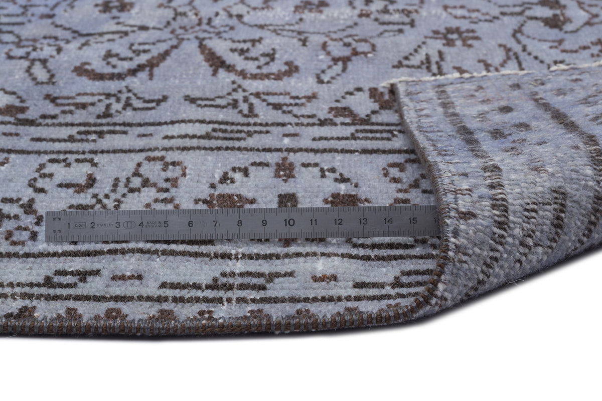 Light blue and brown traditional floral pattern rug with a folded corner and a metal ruler for scale.