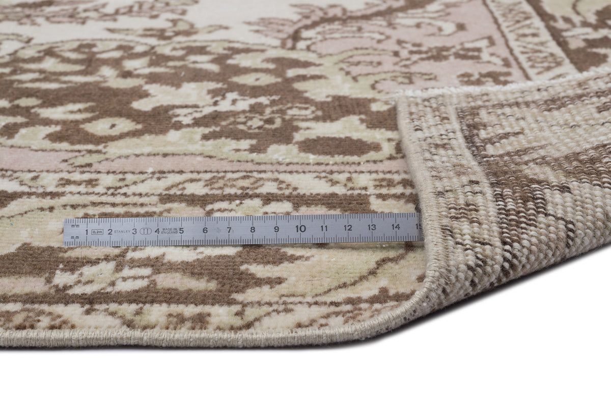 Brown and cream traditional floral rug with a folded corner and a metal ruler for scale on a white background.