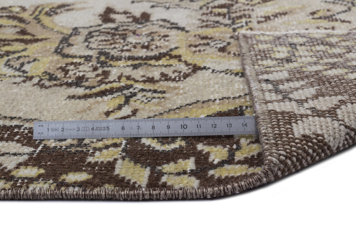 Beige, brown, and yellow vintage-style rug with a floral medallion pattern, shown with a ruler for scale.