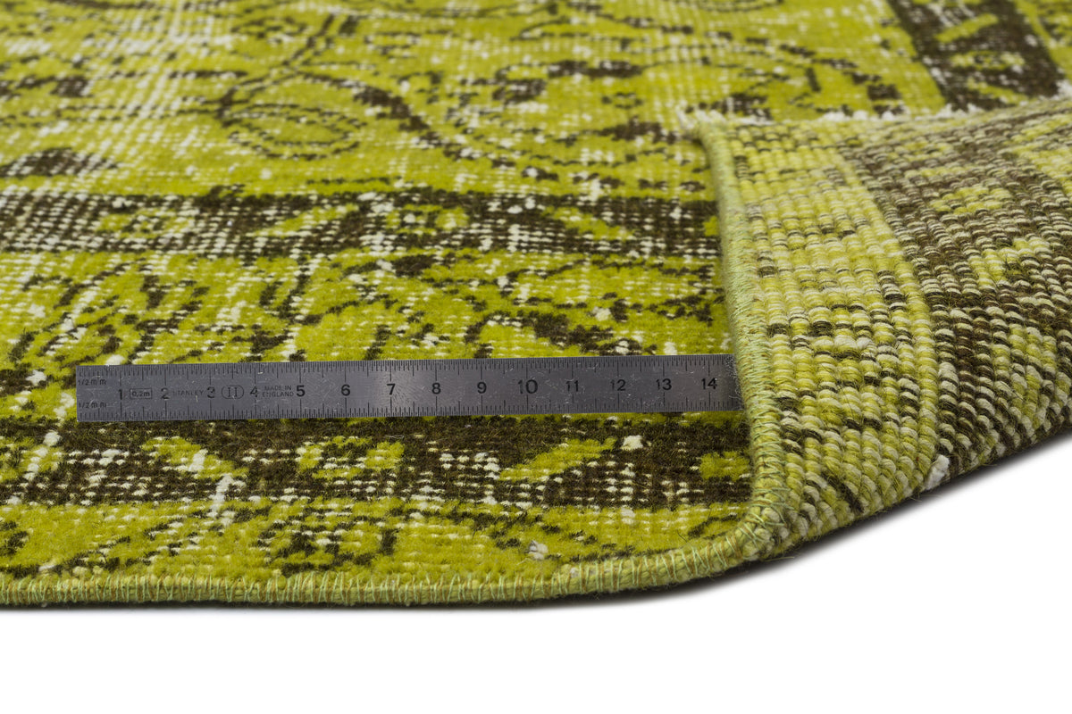 Chartreuse and dark brown distressed medallion rug with a metal ruler showing pile height on a white background.