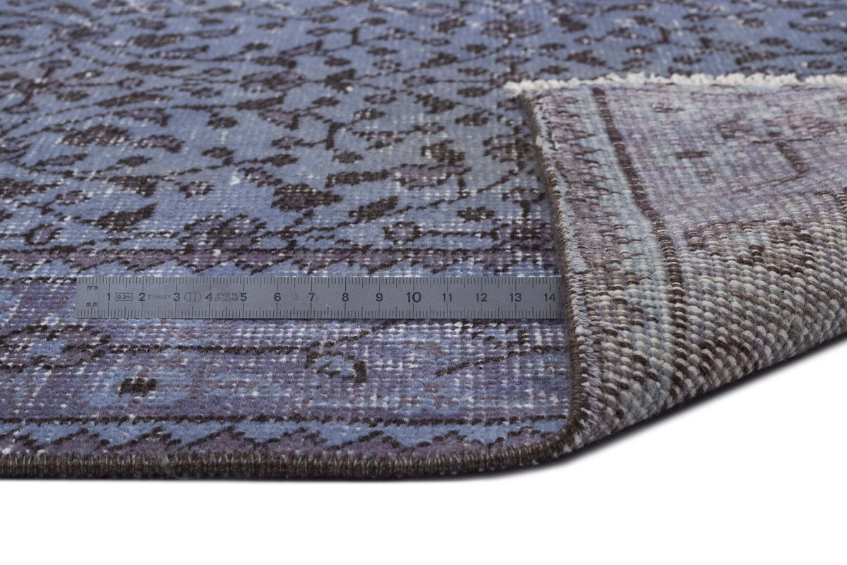 Blue and charcoal distressed floral rug with a folded corner revealing the woven backing and a metal measuring ruler.