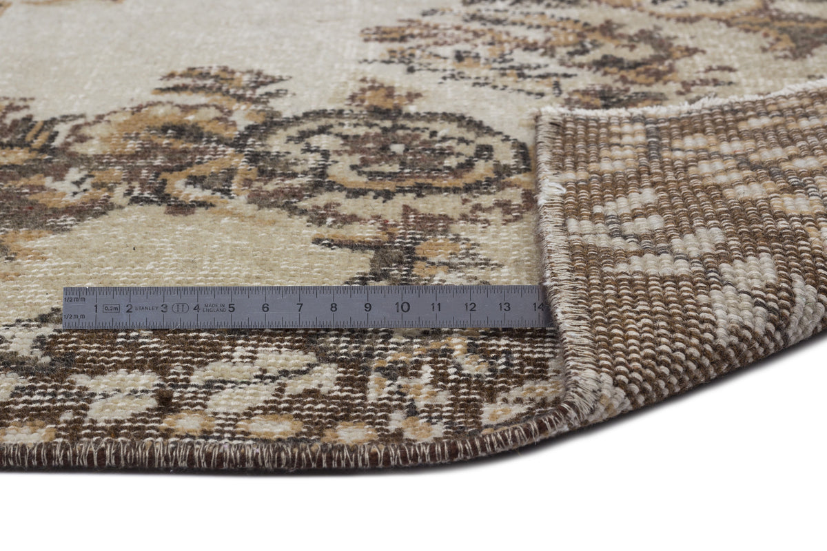 Beige and brown floral medallion rug with a folded corner and a metal ruler for scale on a white background.