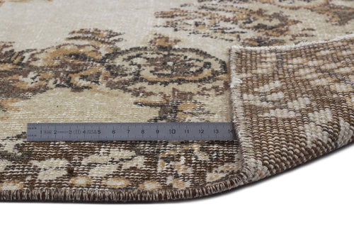 Load image 1 in gallery view. Beige and brown floral medallion rug with a folded corner and a metal ruler for scale on a white background.