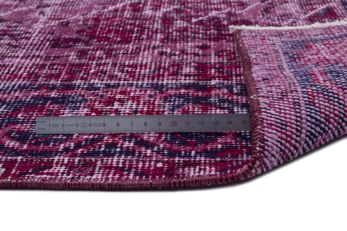 Magenta and dark purple distressed-style rug with a folded corner and a metal ruler for scale.