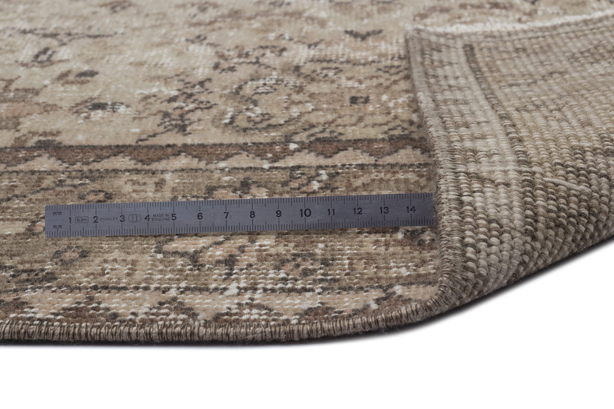 Beige and brown distressed traditional rug with a folded corner and a metal ruler for scale on a white background.