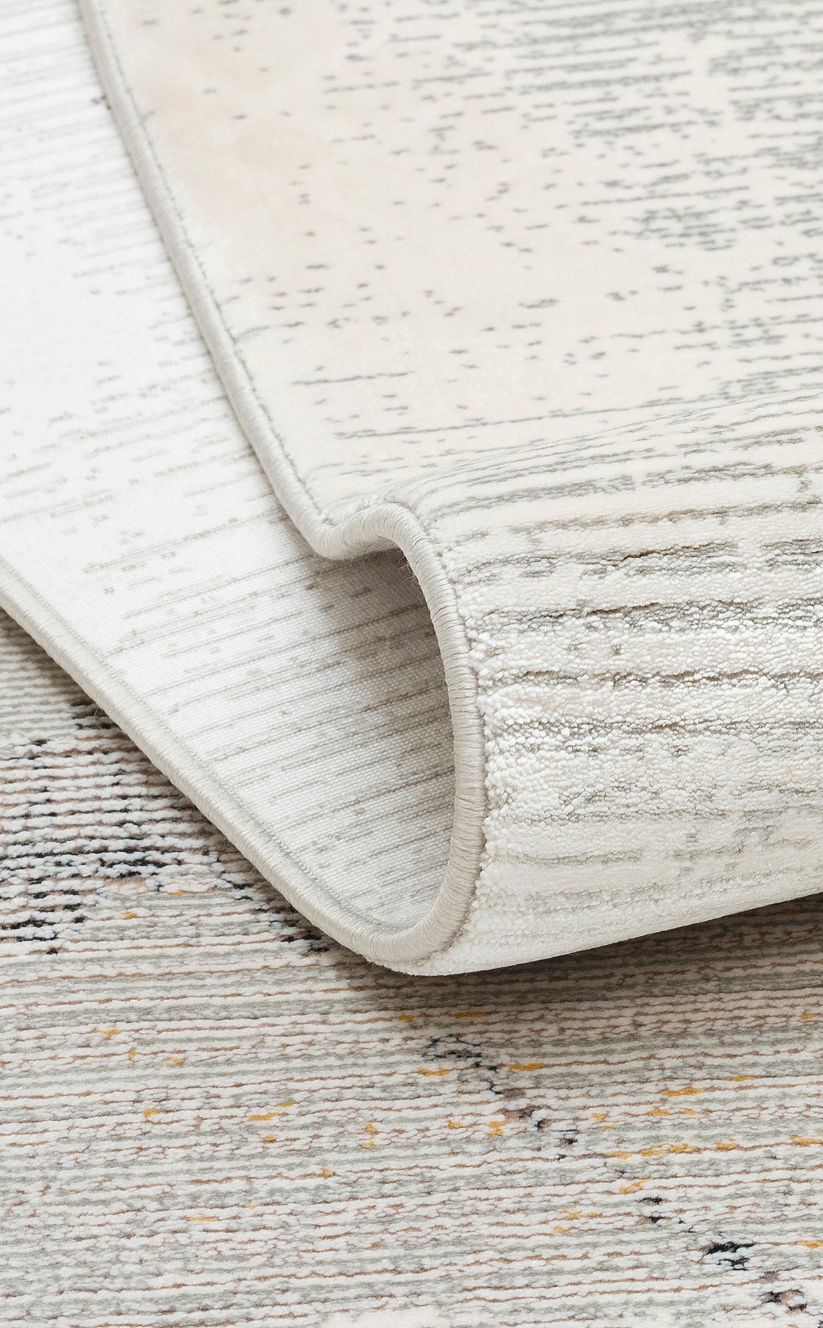 Cream and grey area rug with a distressed linear pattern and subtle yellow accents, shown folded to reveal the texture.