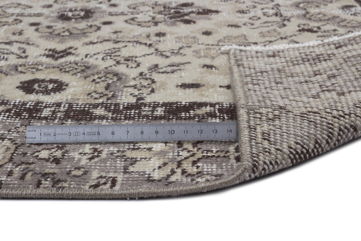 Beige and brown round rug with a distressed floral pattern, showing the woven backing and a metal ruler for scale.