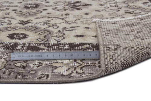 Load image 1 in gallery view. Beige and brown round rug with a distressed floral pattern, showing the woven backing and a metal ruler for scale.