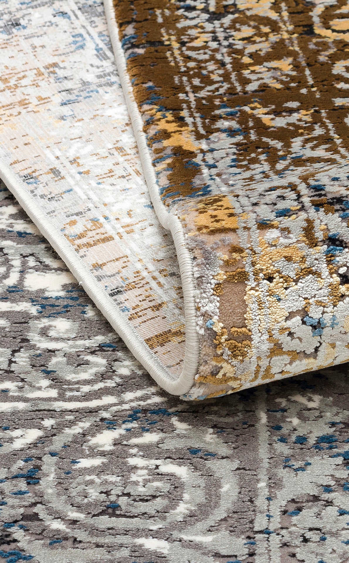 Distressed area rug with a folded corner, featuring a brown, grey, and blue abstract medallion pattern.