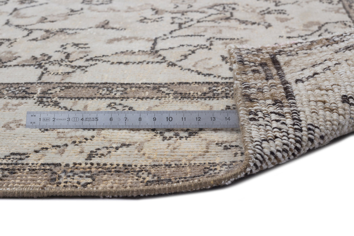 Beige and charcoal distressed floral rug with a curled corner and a metal ruler showing scale on a white background.