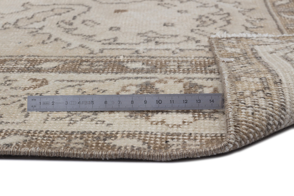 Beige and cream vintage-style rug with a faded floral pattern, shown with a metal ruler for scale.