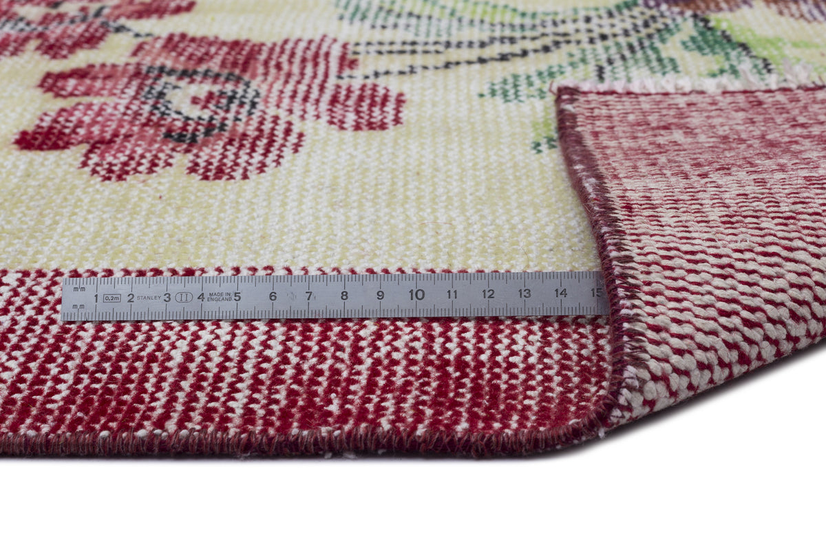 Cream rug with red floral pattern and a folded corner showing the red underside, measured by a metal ruler.