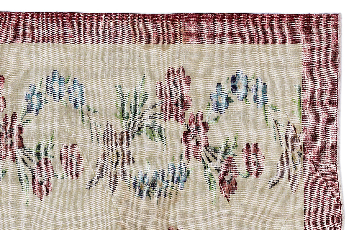 Beige rug with a red border and a repeating floral pattern in red, blue, and green on a white background.