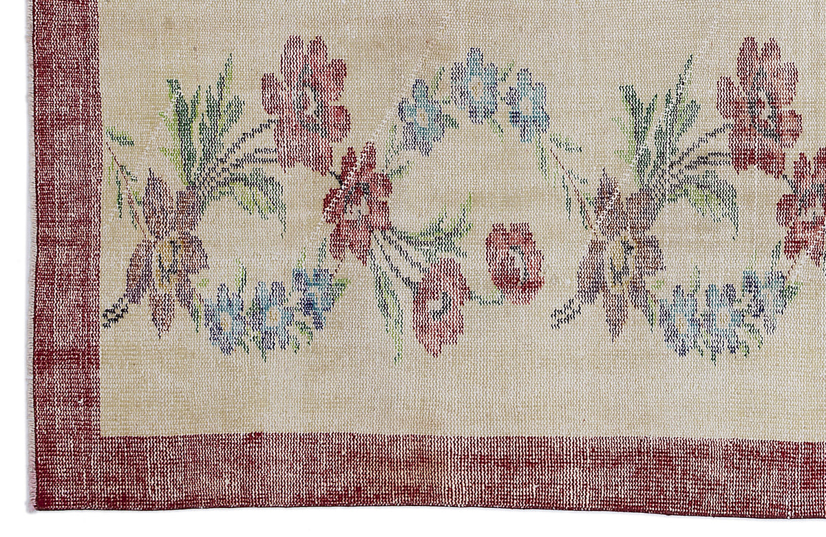 Beige rug with a red border and a central floral pattern in red, blue, and green.