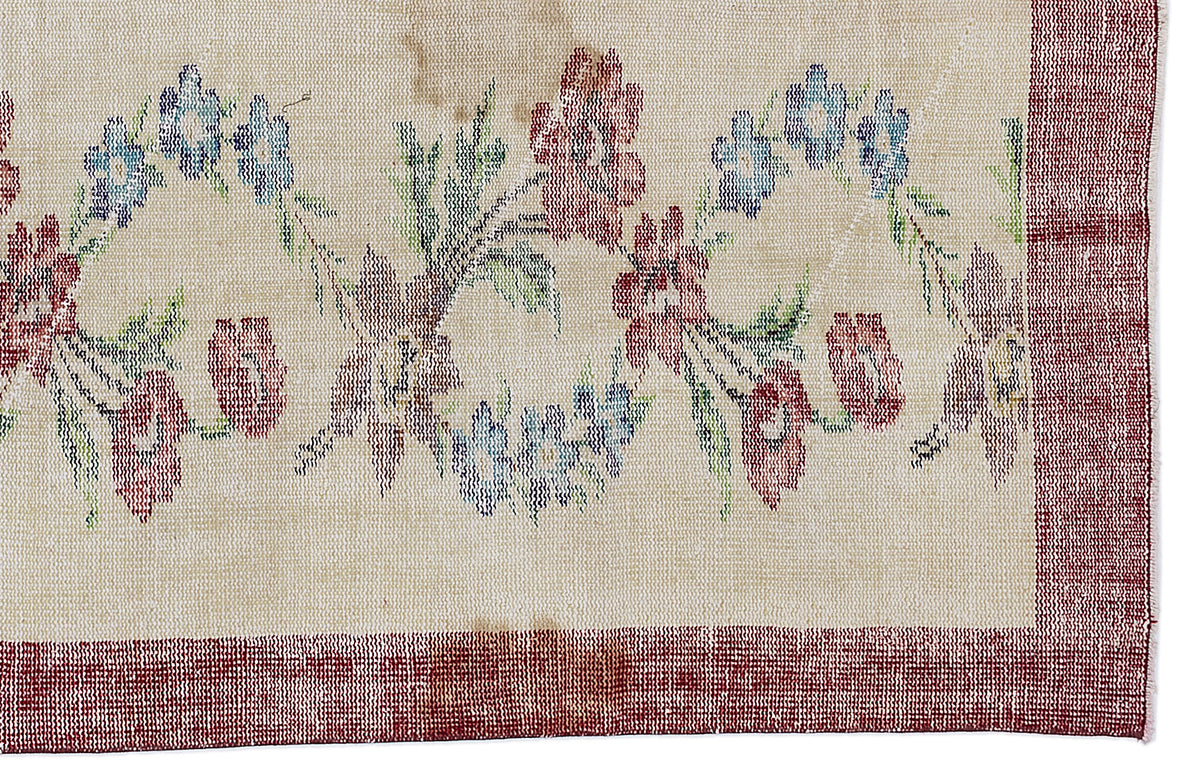 Beige rug with a red border and a floral pattern in red, blue, and green.