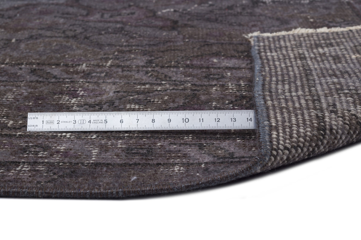 Dark charcoal distressed rug with a faded traditional pattern, shown with a metal ruler for scale on a white background.
