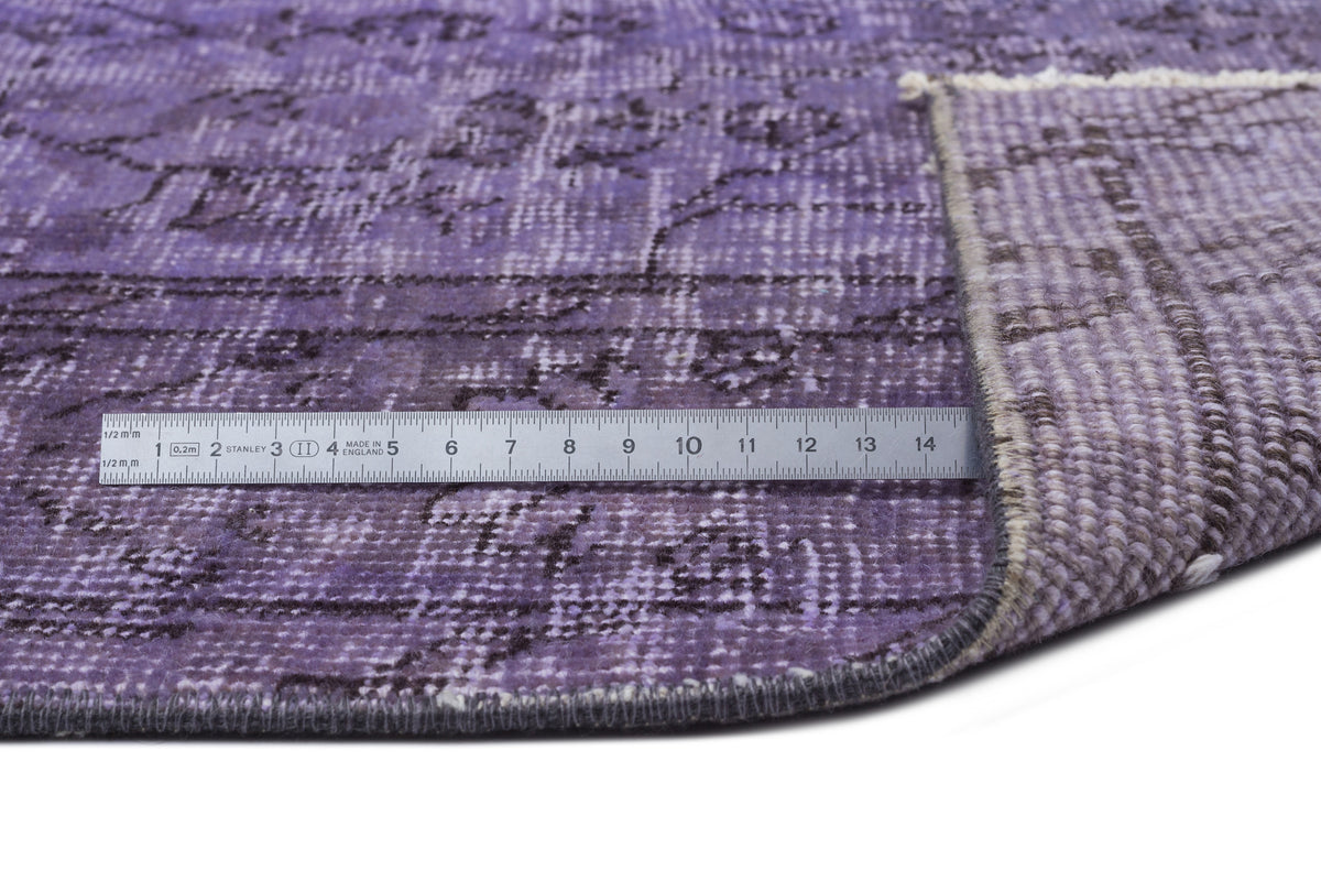 Distressed purple rug with a dark grey floral pattern, shown with a metal ruler for scale on a white background.