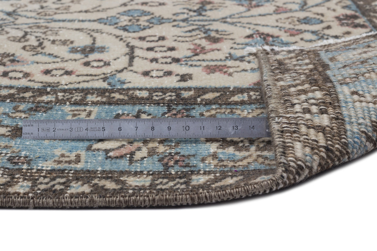 Beige, blue, and brown traditional floral rug with a folded corner and a metal ruler showing scale on a white background.