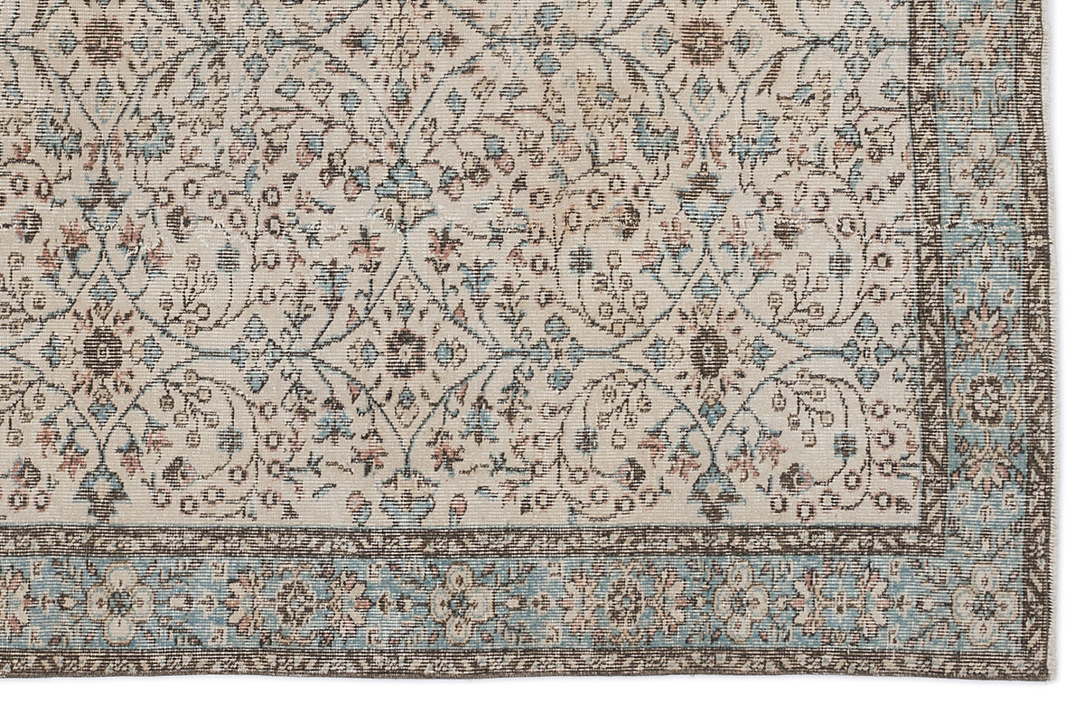 Cream rug with a distressed floral trellis pattern in muted blue, brown, and pink, featuring a wide decorative border.