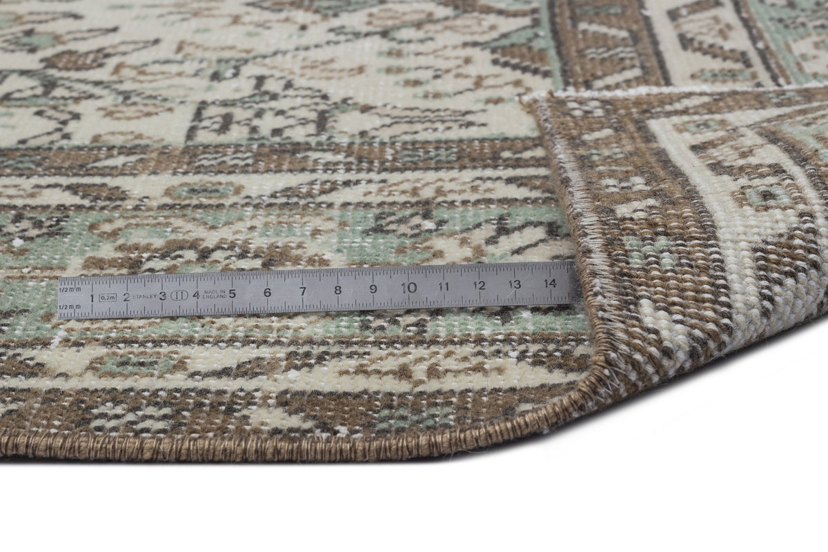 Beige, brown, and sage green traditional patterned rug with a folded corner and a metal ruler for scale.
