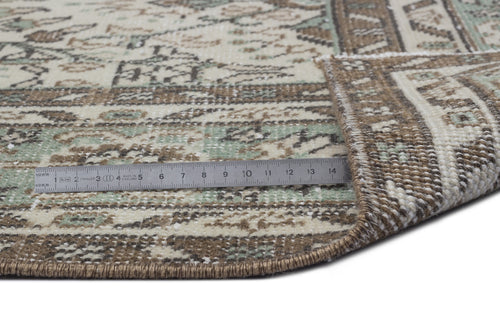 Load image 1 in gallery view. Beige, brown, and sage green traditional patterned rug with a folded corner and a metal ruler for scale.