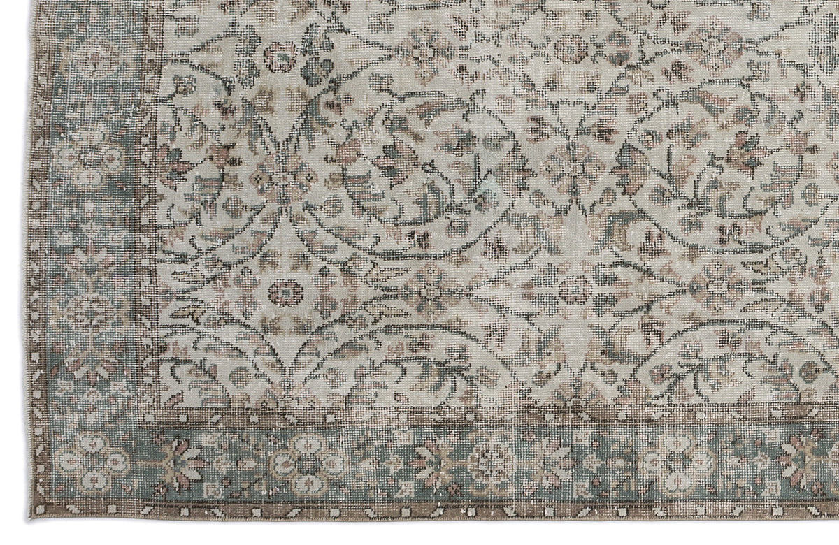 Distressed beige rug with a faded floral medallion pattern in muted sage green and dusty rose, featuring a wide border.