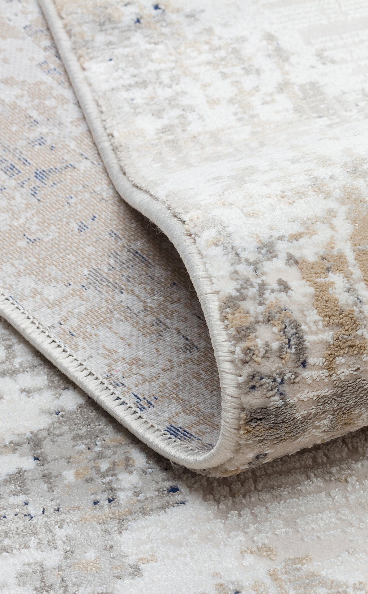 Cream, beige, and grey area rug with a distressed, abstract pattern, shown folded to reveal the serged edge.