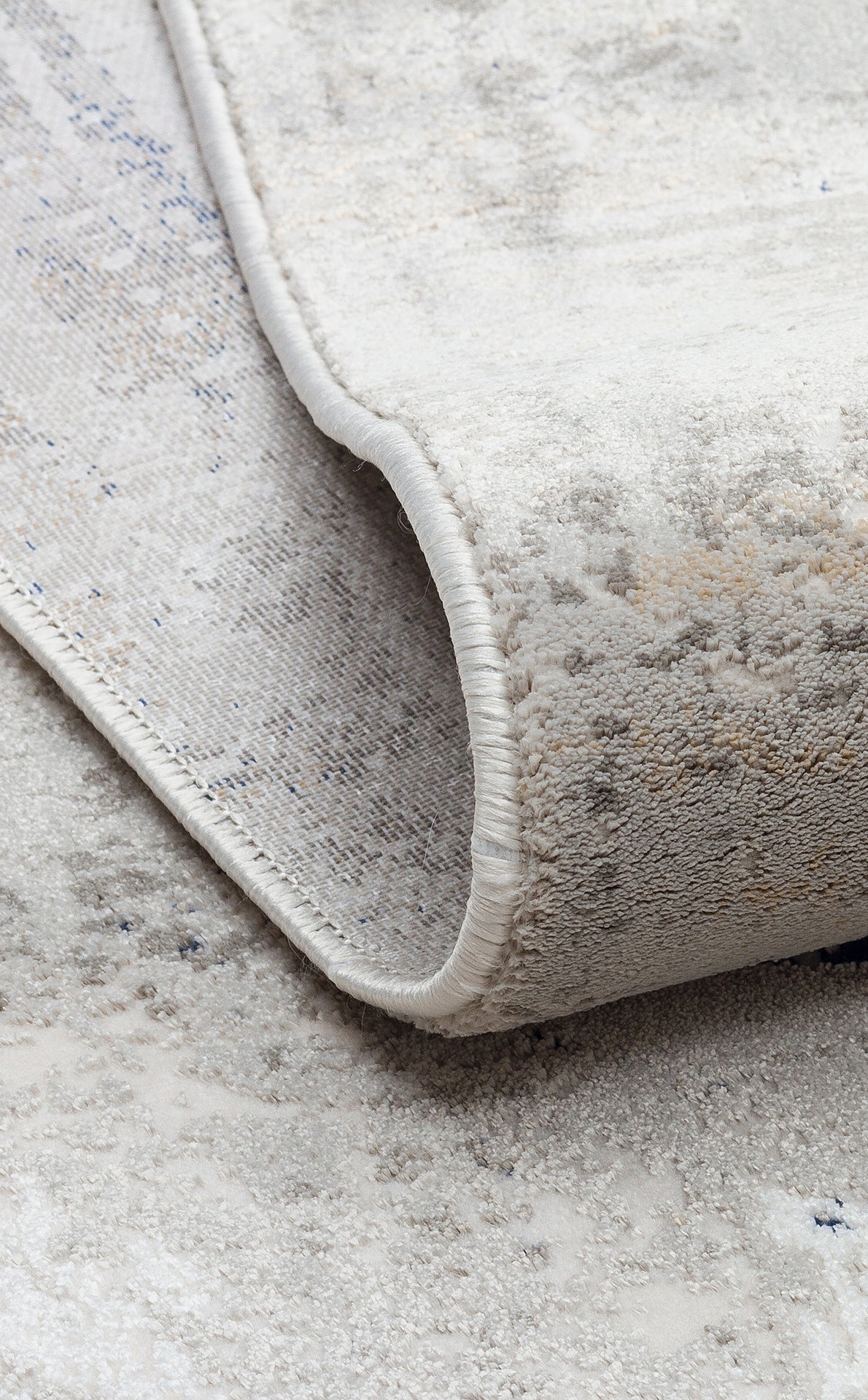 Cream and grey area rug with a distressed, abstract pattern and a finished serged edge.