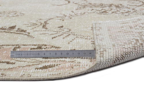 Load image 1 in gallery view. Beige and cream round rug with a distressed floral pattern, shown with a metal ruler for scale on a white background.