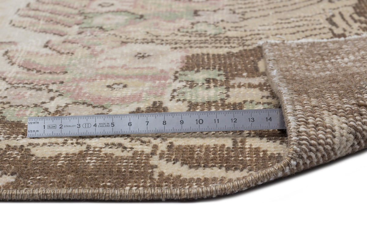 Beige, brown, and muted pink vintage-style rug with a floral medallion pattern, shown with a metal ruler for scale.