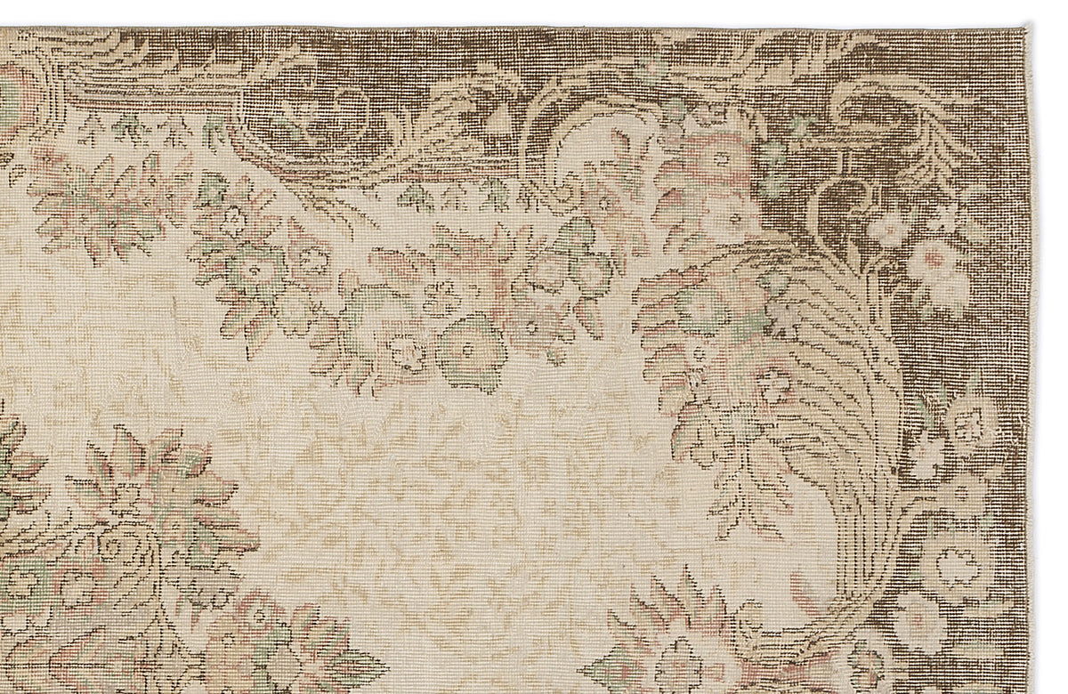 Beige rug with a dark brown border and muted floral medallion pattern in faded pink and sage green.