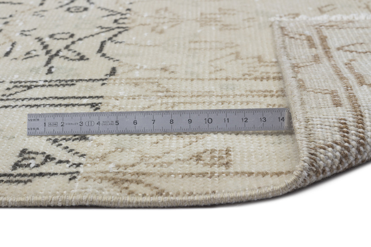 Beige and cream vintage-style rug with a faded charcoal geometric pattern, shown with a metal ruler for scale.