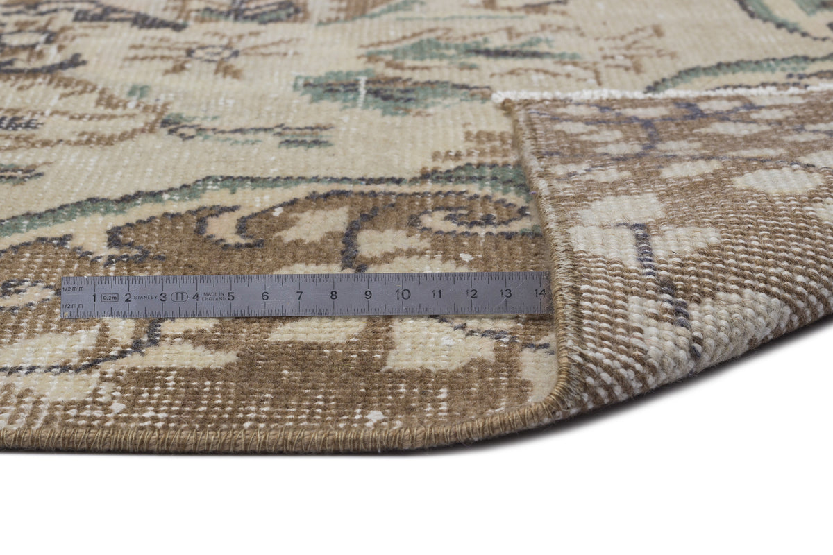 Beige, brown, and sage green vintage-style rug with a floral pattern, shown with a metal ruler measuring the pile.