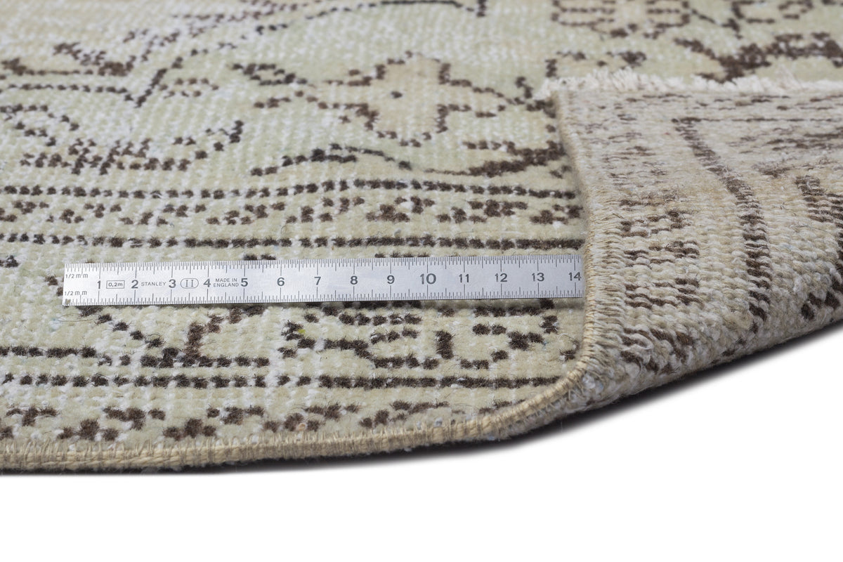 Beige and brown vintage-style rug with a distressed floral pattern, shown with a metal ruler for scale.
