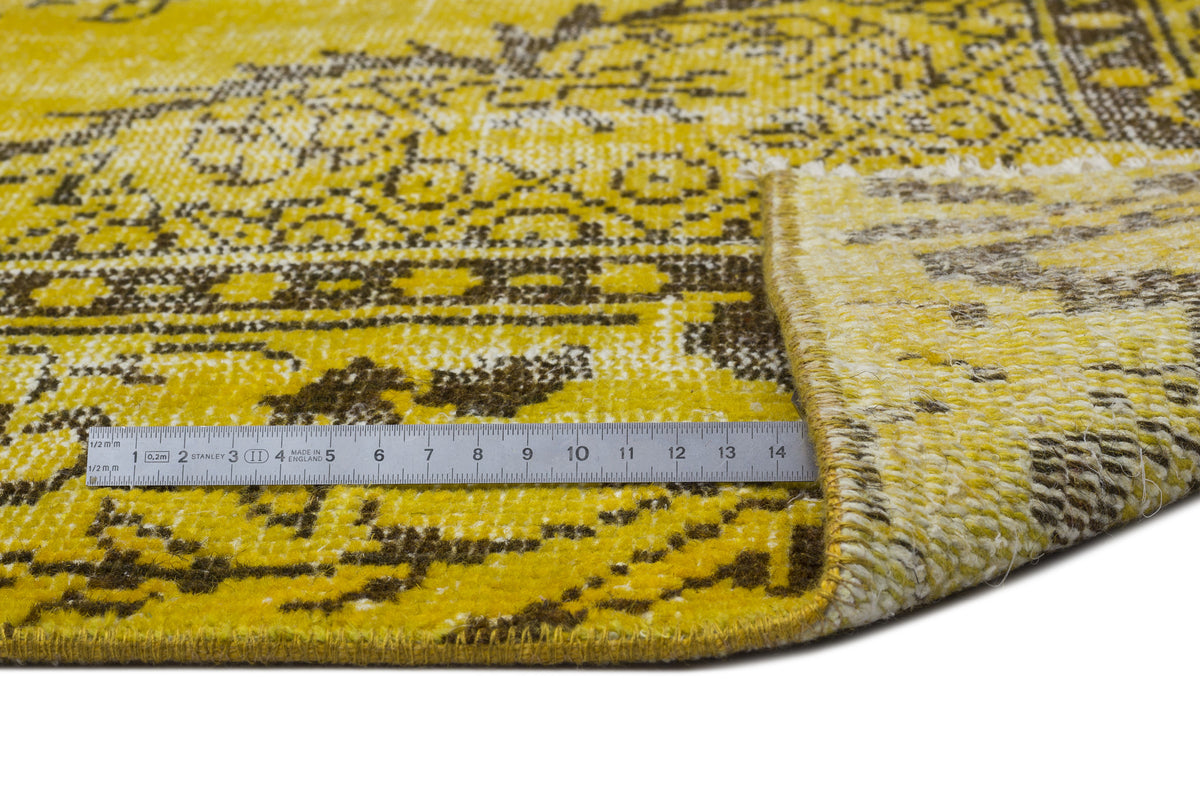 Yellow and brown distressed rug with a traditional medallion pattern, shown with a metal ruler for scale.