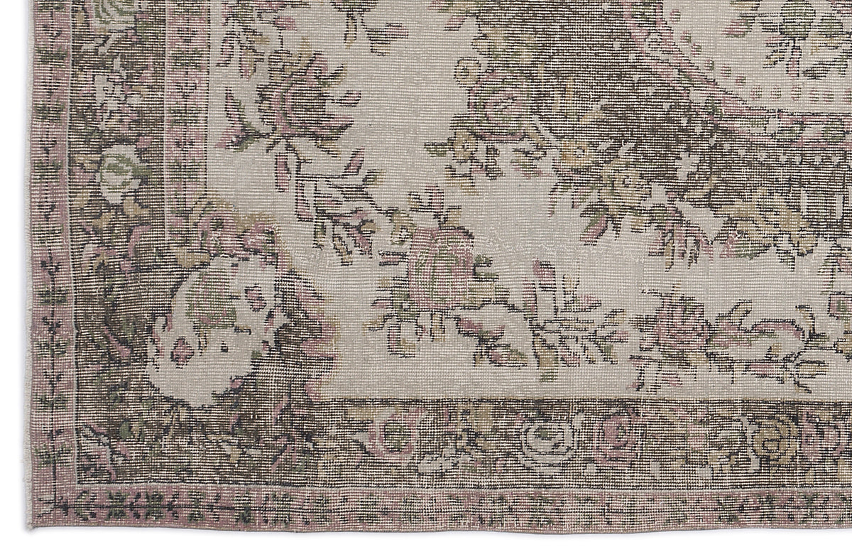 Distressed beige rug with a faded floral medallion pattern in muted pink, olive green, and charcoal grey.