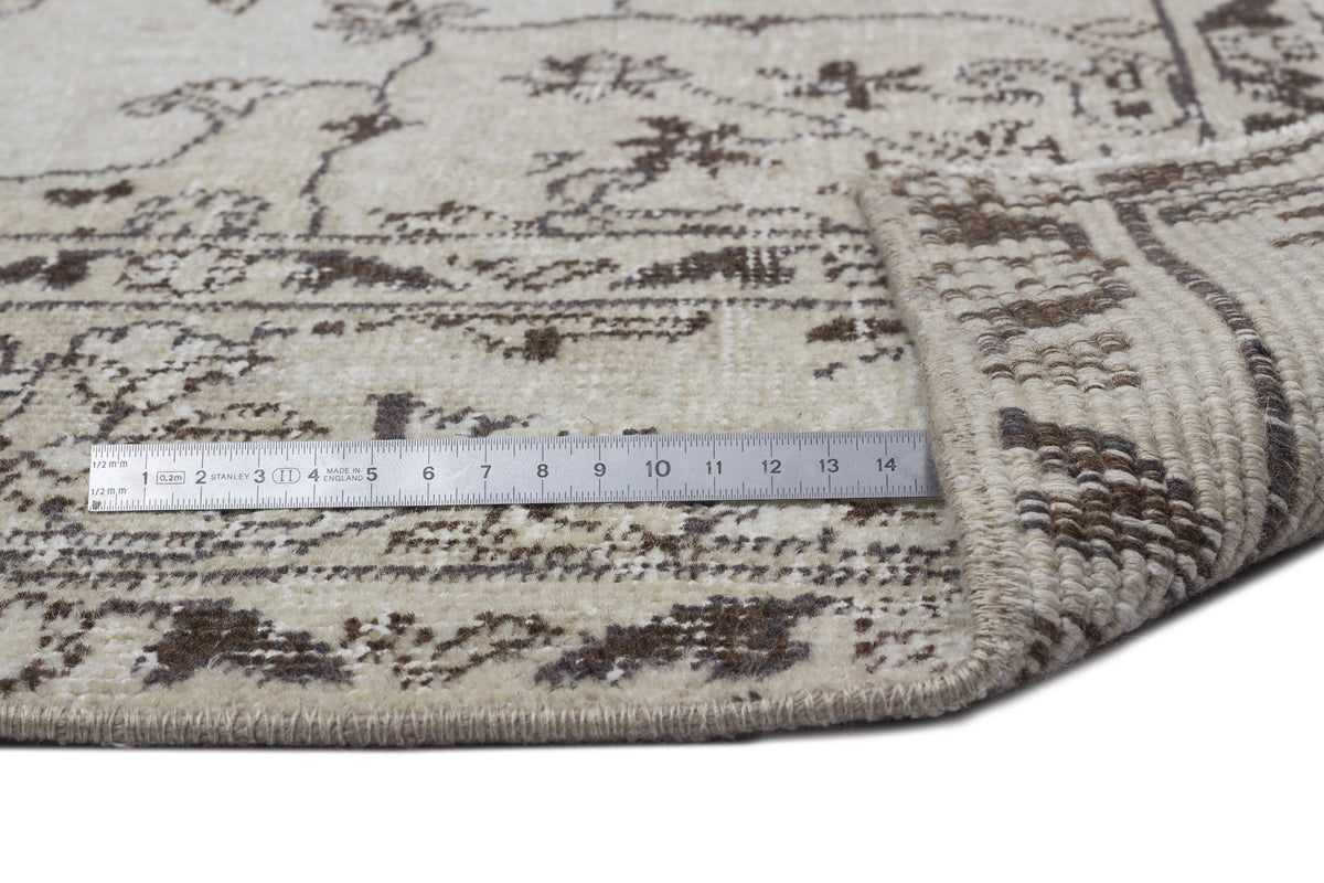 Beige and brown rug with a distressed traditional pattern, shown with a metal ruler for scale on a white background.