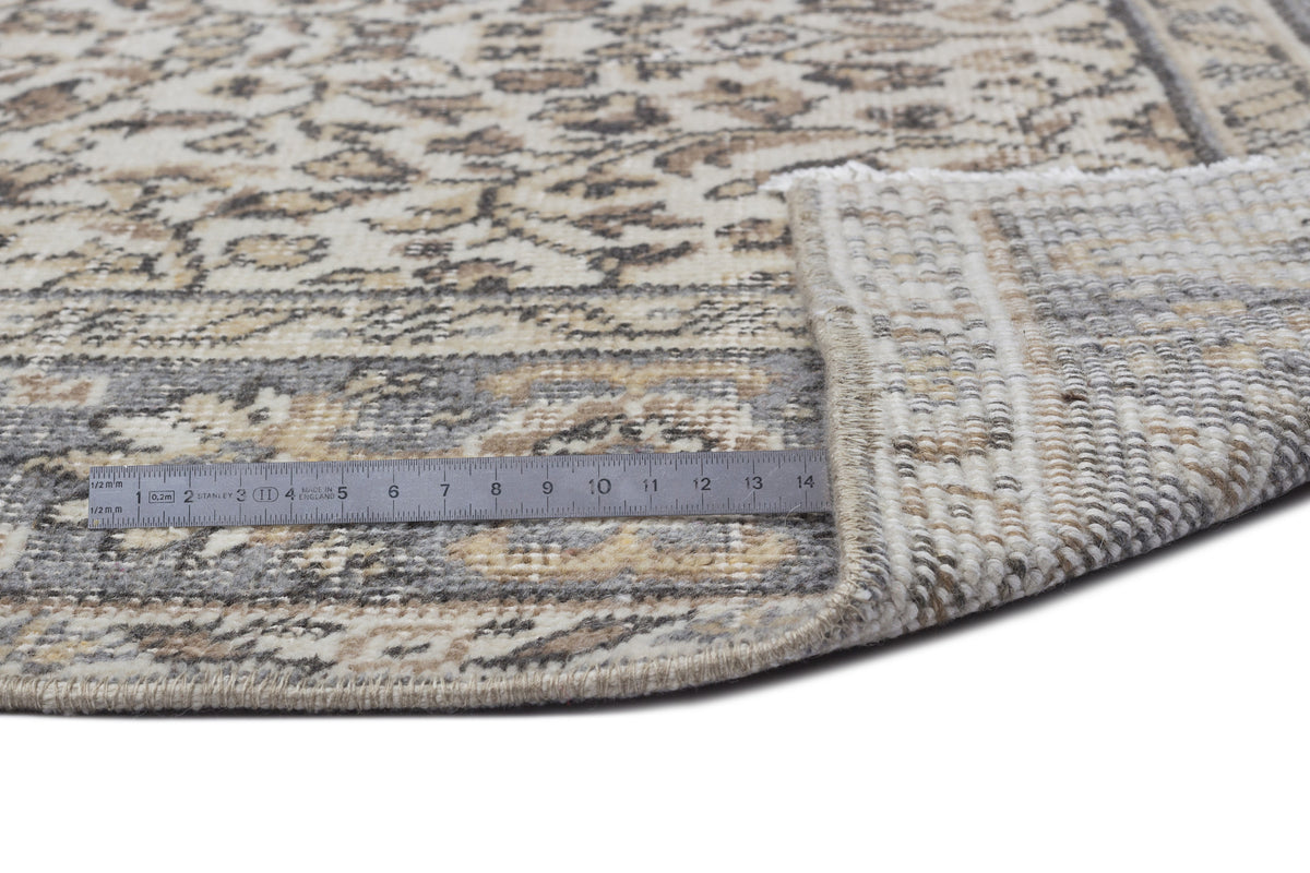 Beige and grey round rug with a distressed floral pattern, shown with a metal ruler for scale on a white background.