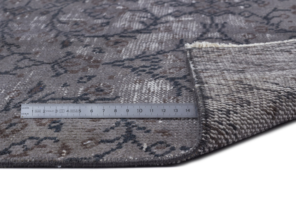 Grey and charcoal distressed floral rug with a folded corner and a metal ruler for scale on a white background.